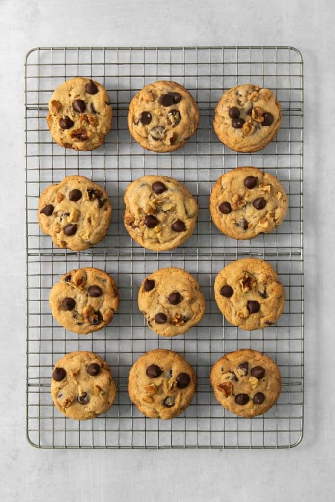 A dozen baked walnut chocolate chip cookies on a cooling rack.