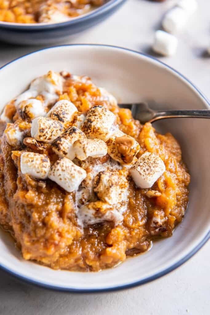 A close up view of a single serving of sweet potato casserole in a bowl with a fork.