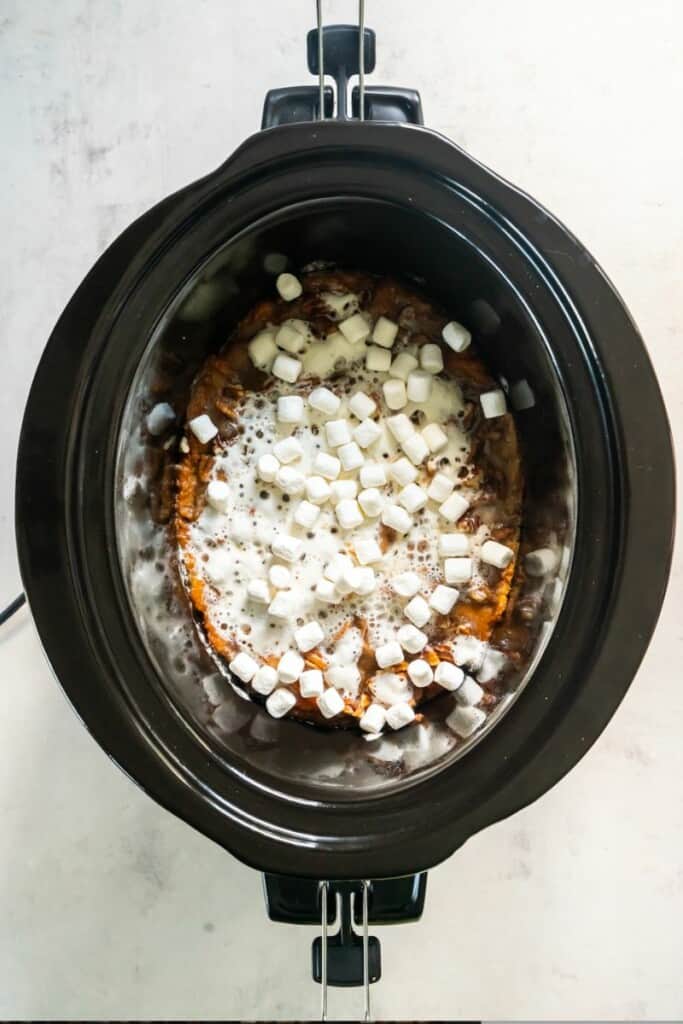 Adding marshmallows to mashed sweet potato mixture in a black crock pot.