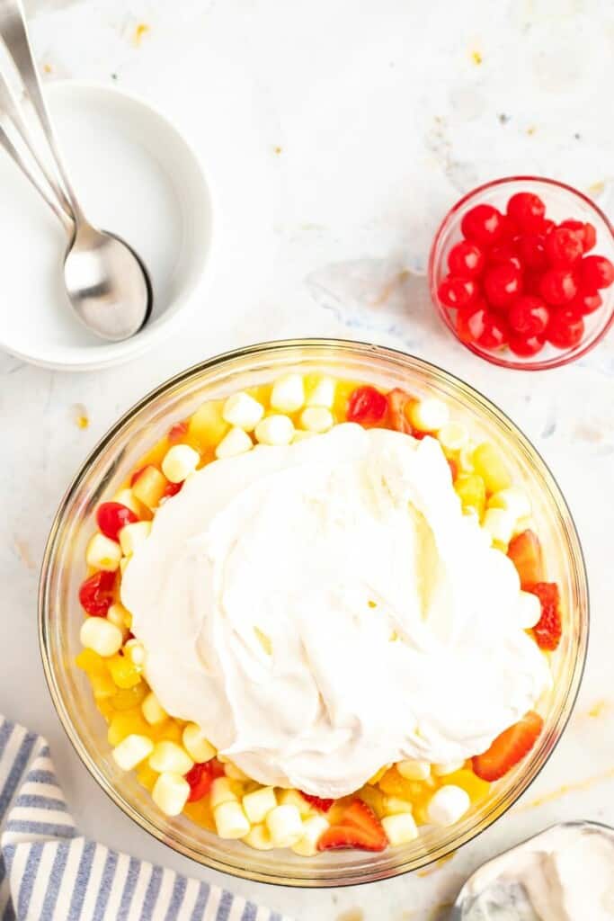 Adding in Cool Whip to the mixed fruit salad in a bowl. 