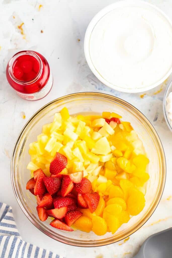 Adding chopped fruit to bowl with pineapple vanilla pudding.