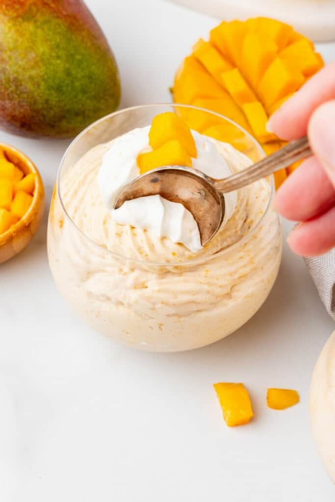 Dipping a spoon into the mango mousse filled dessert dish to remove a bite.