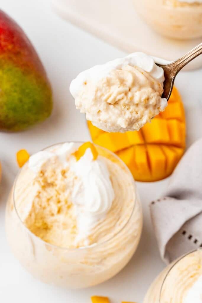 A spoon holding a bite of mango mousse over the dessert dish.