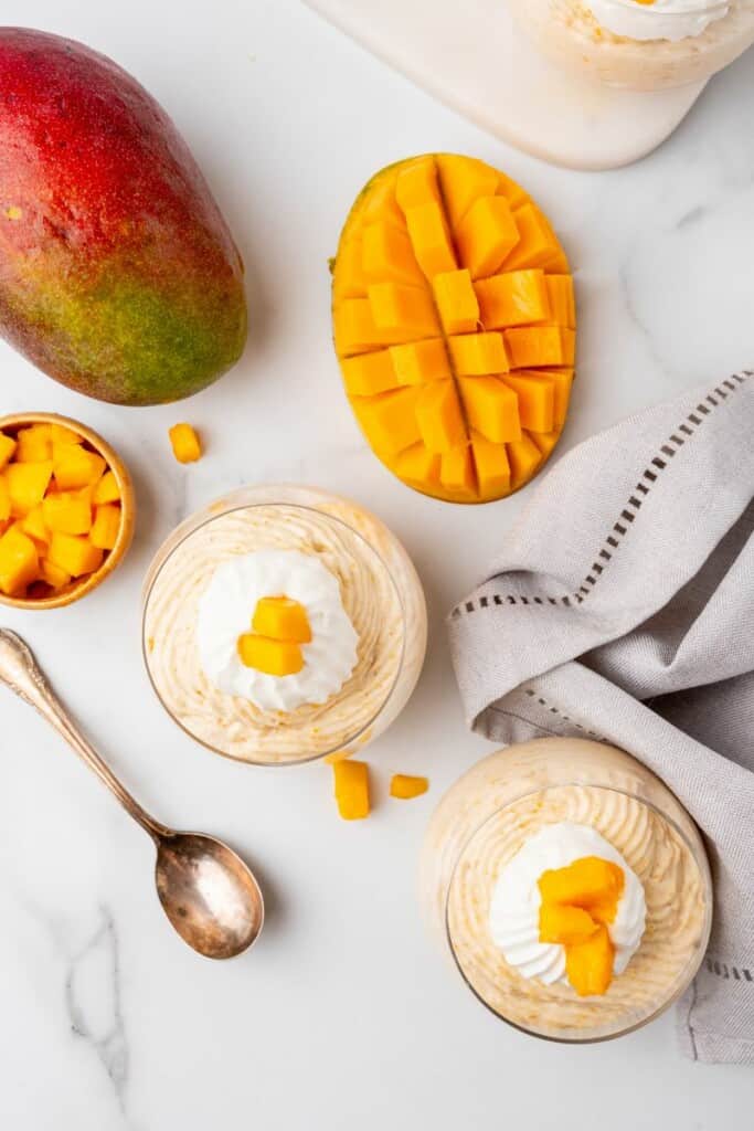 Overhead view of two dessert bowls of mango mousse with additional pieces of mango in the background.