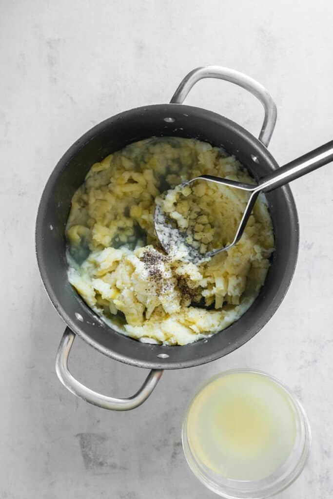 Mashing cooked potatoes with a potato masher in a pot. 