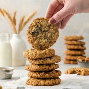 holding an oatmeal cranberry cookie over a stack of cookies.