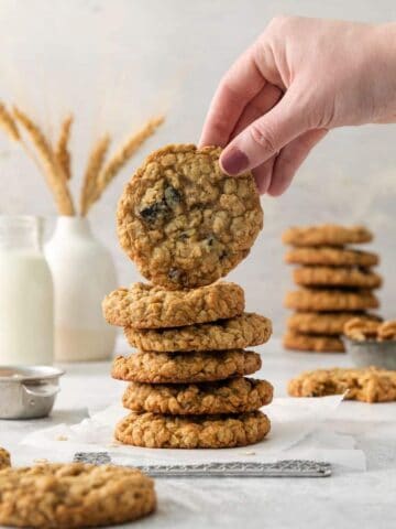 holding an oatmeal cranberry cookie over a stack of cookies.