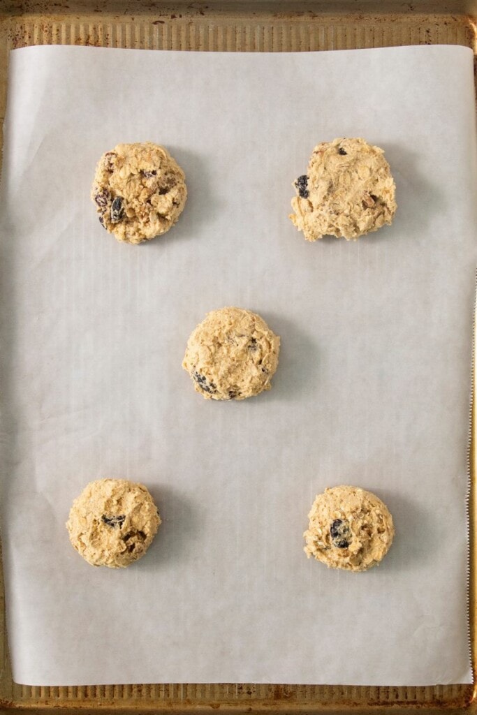 adding dollops of oatmeal cookie batter to parchment paper on sheet pan. 