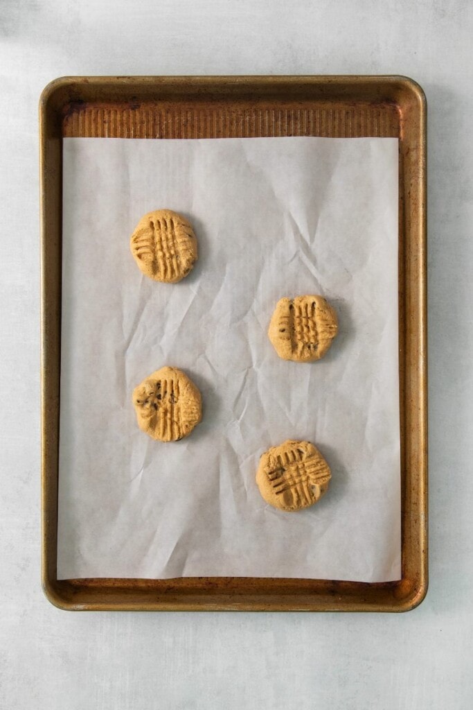Four chocolate chip peanut butter cookie dough pieces on a parchment lined baking sheet.