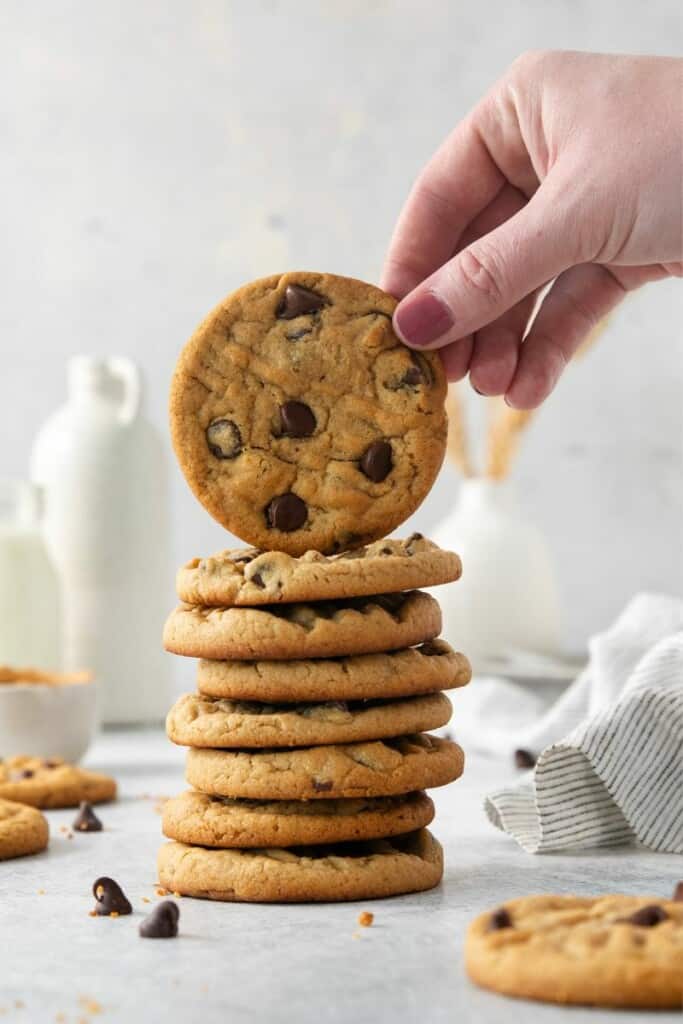 Eight vertically stacked chocolate chip peanut butter cookies with another cookie being held upright by a hand.