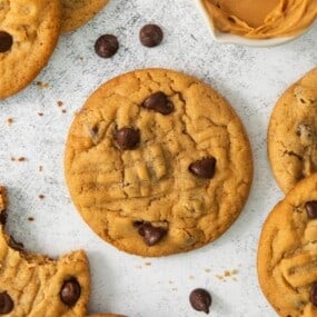 Chocolate Chip Peanut Butter Cookies resting on a flat surface with chocolate chips sprinkled around.