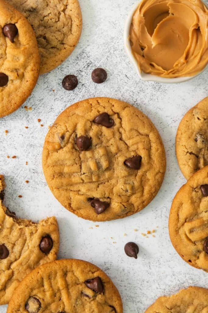 Chocolate Chip Peanut Butter Cookies resting on a flat surface with chocolate chips sprinkled around.