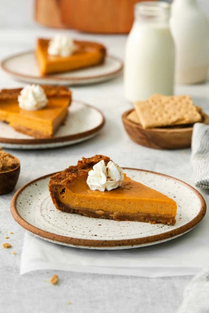 A side view of a slice of sweet potato pie topped with whipped cream. Additional slices in the background.