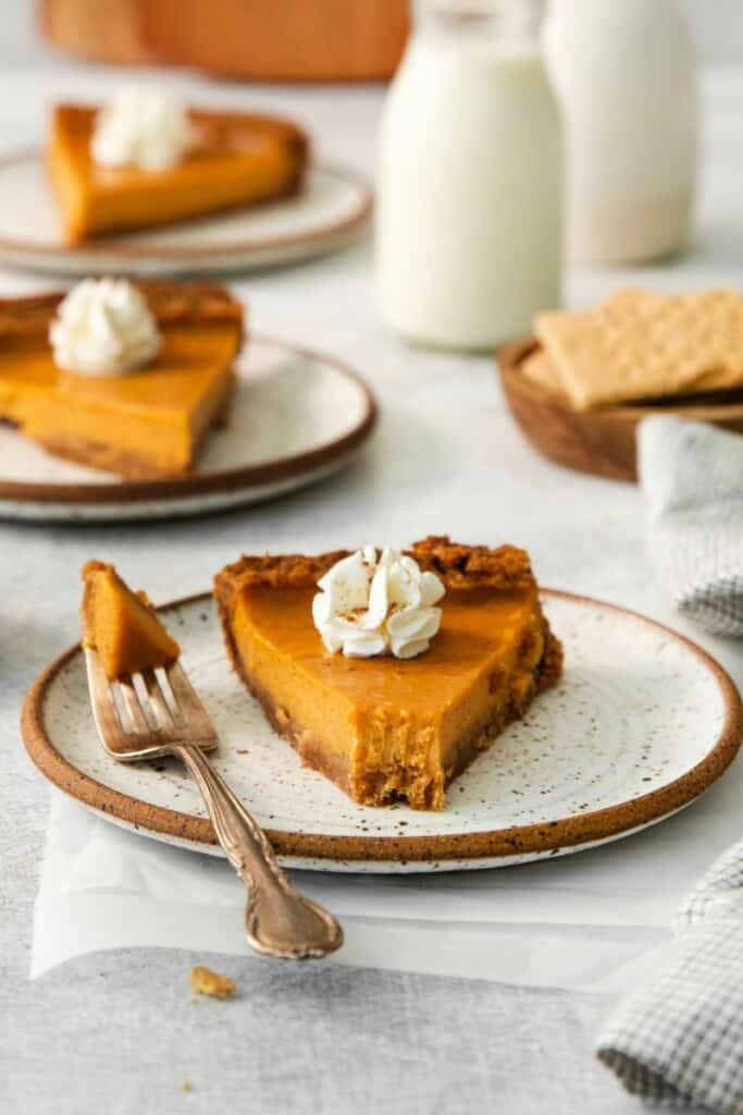 A slice of sweet potato pie topped with whipped cream. One bite removed with a fork resting on the saucer.