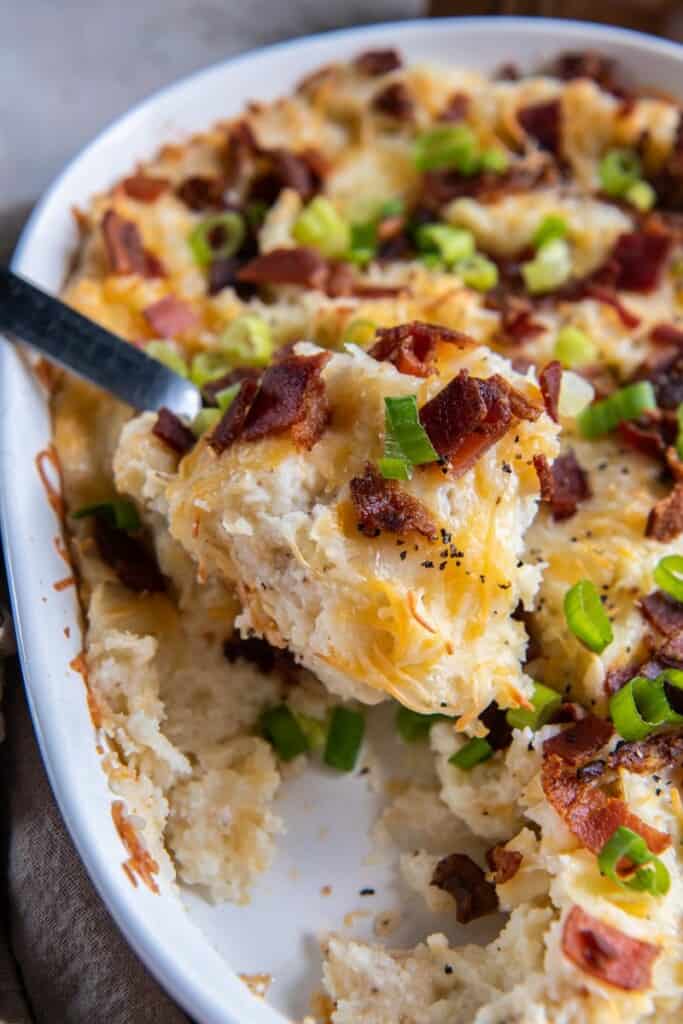 A close up view of a spoon holding a bite of twice baked mashed potatoes.