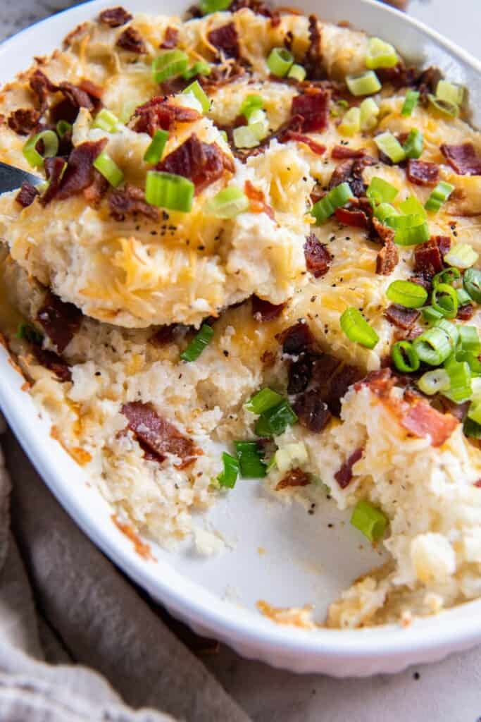 A close up view of the baked twice baked mashed potatoes dish with one serving removed.