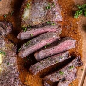 Overhead view of air fryer new york strip steak cut into strips with a dab of butter on top of an uncut steak.