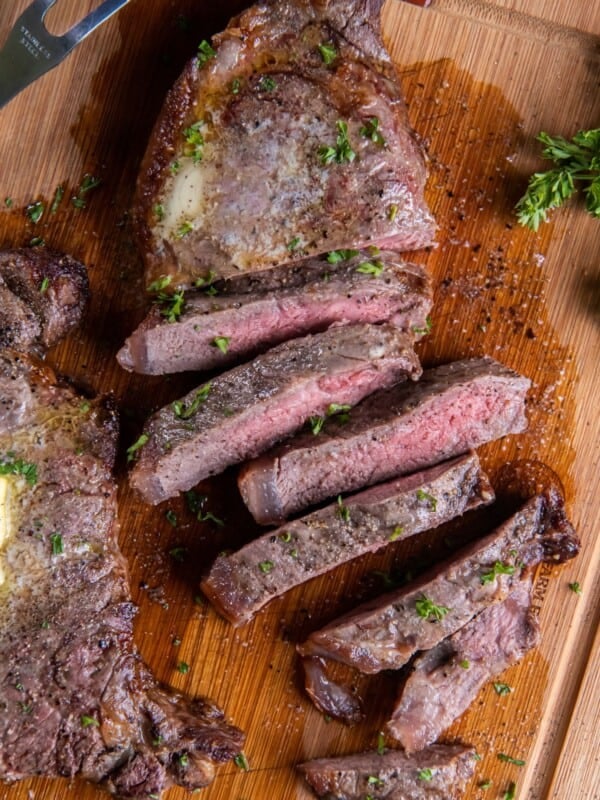 Overhead view of air fryer new york strip steak cut into strips with a dab of butter on top of an uncut steak.
