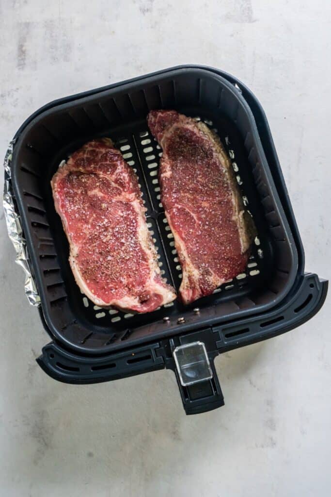Raw new york strip in an air fryer basket ready to be cooked.