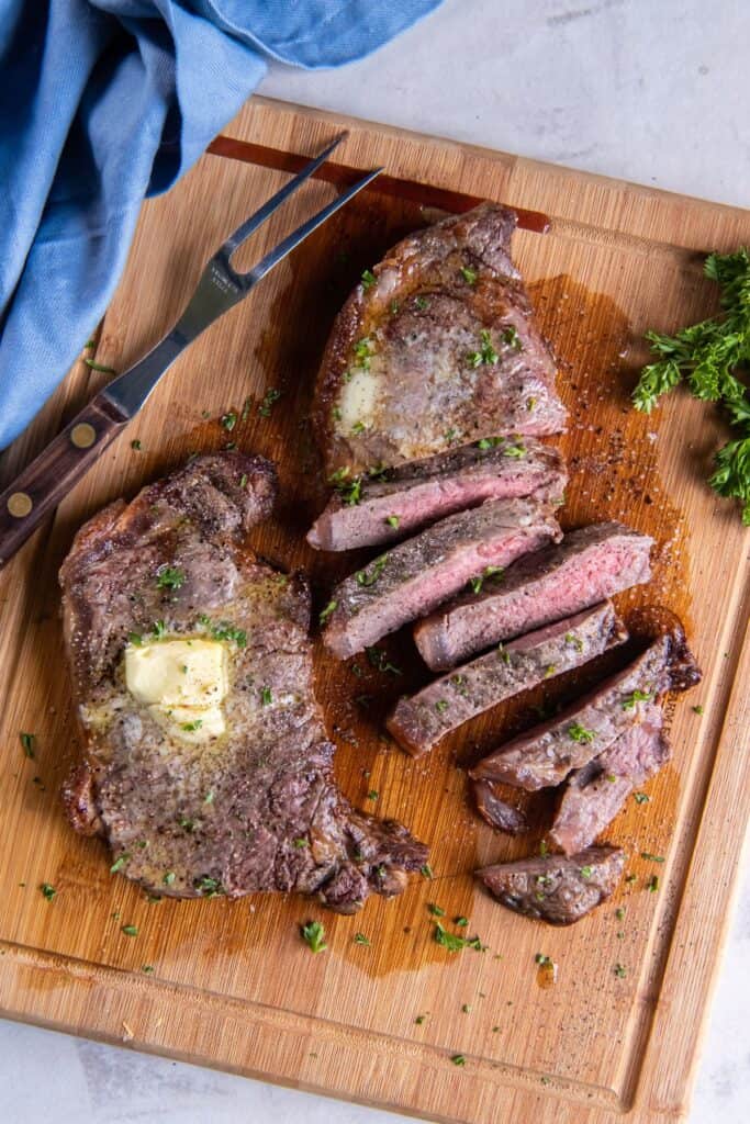 Overhead view of air fryer new york strip steak cut into strips with a dab of butter on top of an uncut steak.
