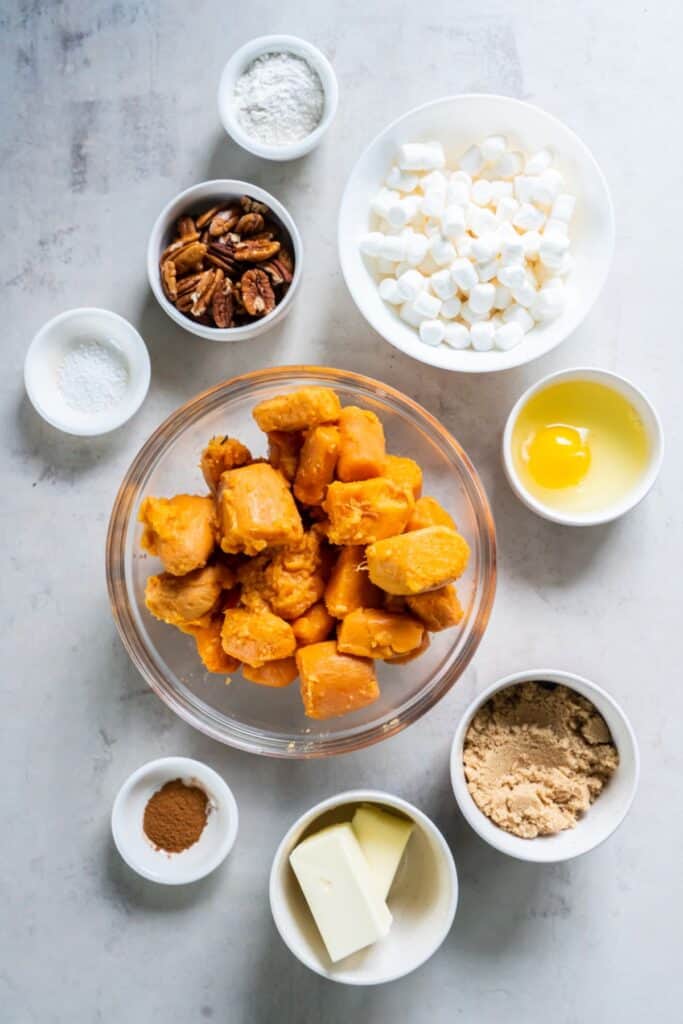 Ingredients needed to make crock pot sweet potato casserole: canned yams, butter, brown sugar, egg, cinnamon, salt, pecans, flour, and mini marshmallows.