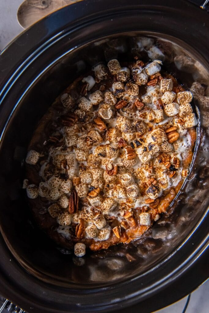 Cooked sweet potato casserole in a crock pot with the marshmallows browned on top.