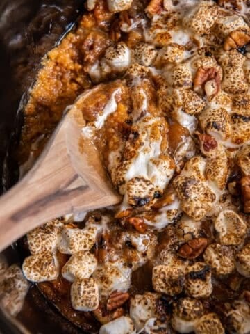 Close up of the crock pot sweet potato casserole with a wooden serving spoon in it.