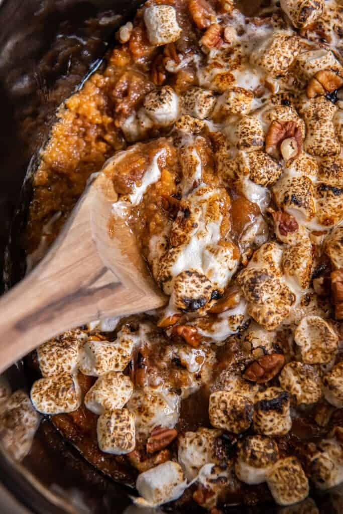 Close up of the crock pot sweet potato casserole with a wooden serving spoon in it.