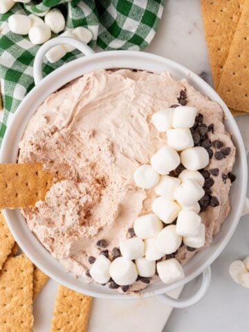 Hot cocoa dip topped with marshmallows and chocolate chips with a graham cracker dipped in it.