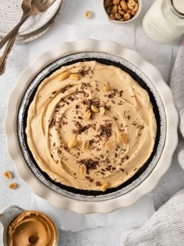 Peanut butter pie with cool whip in an Oreo crust topped with peanuts and chocolate shavings.