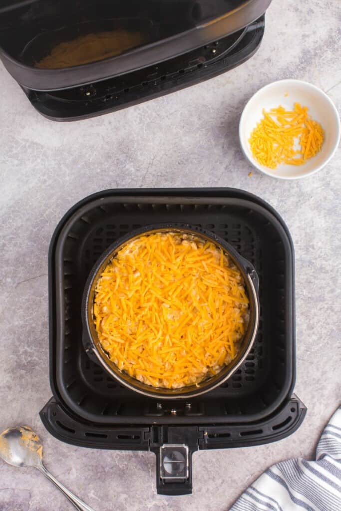 adding a layer of shredded cheese to cooked mac and cheese