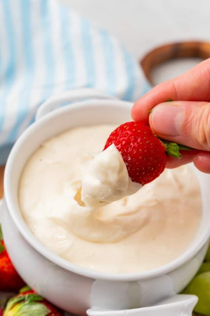 taking a bite our of fresh fruit with some cream cheese fruit dip with powdered sugar.