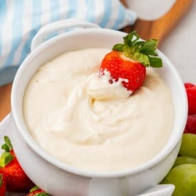 dipping a strawberry into cream cheese fruit dip recipe.