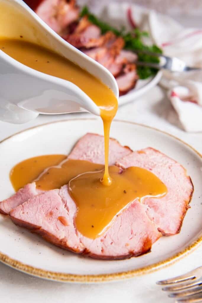 pouring ham gravy over slices of ham on a plate.