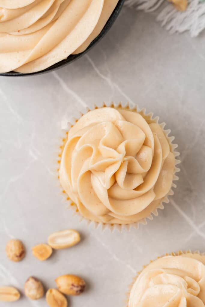 Piping peanut butter cream cheese frosting to a vanilla cupcake. 
