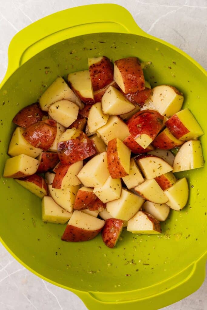 Red potatoes in a green bowl tossed with seasonings and oil.