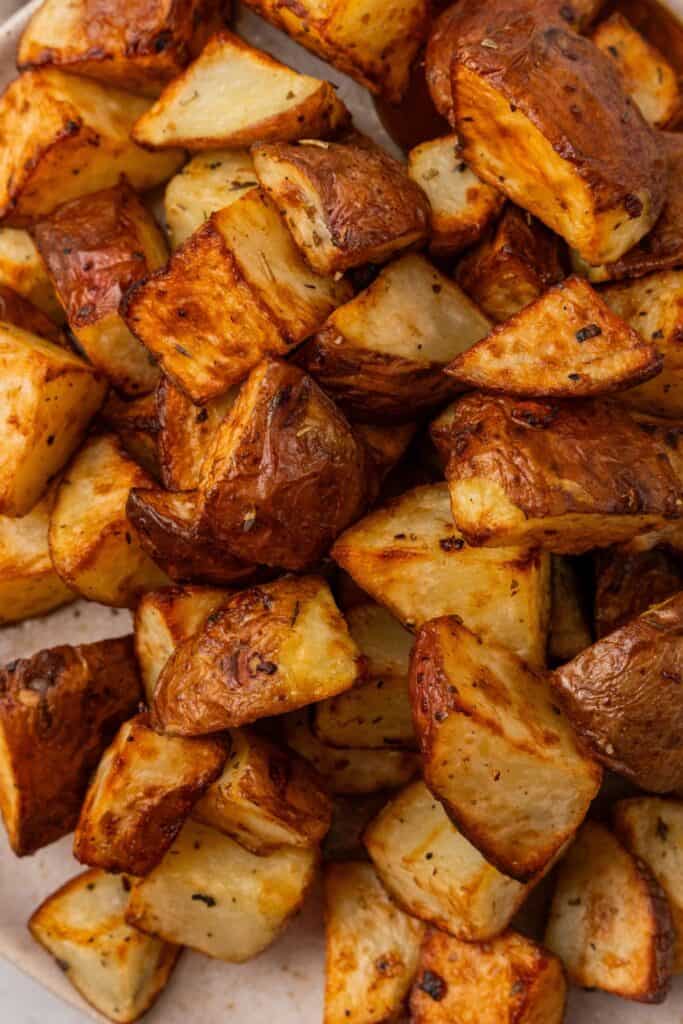 Close up of air fryer red potatoes on a white plate, showing golden brown and roasted.