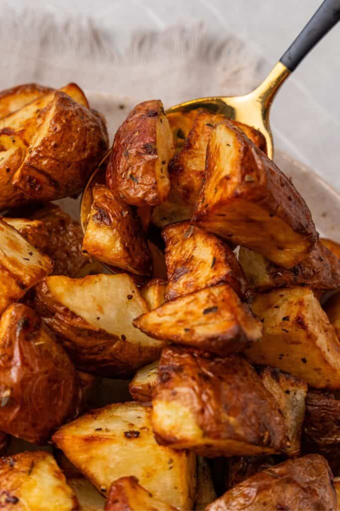 Air fry red potatoes on a white plate with some being picked up slightly with a spoon.