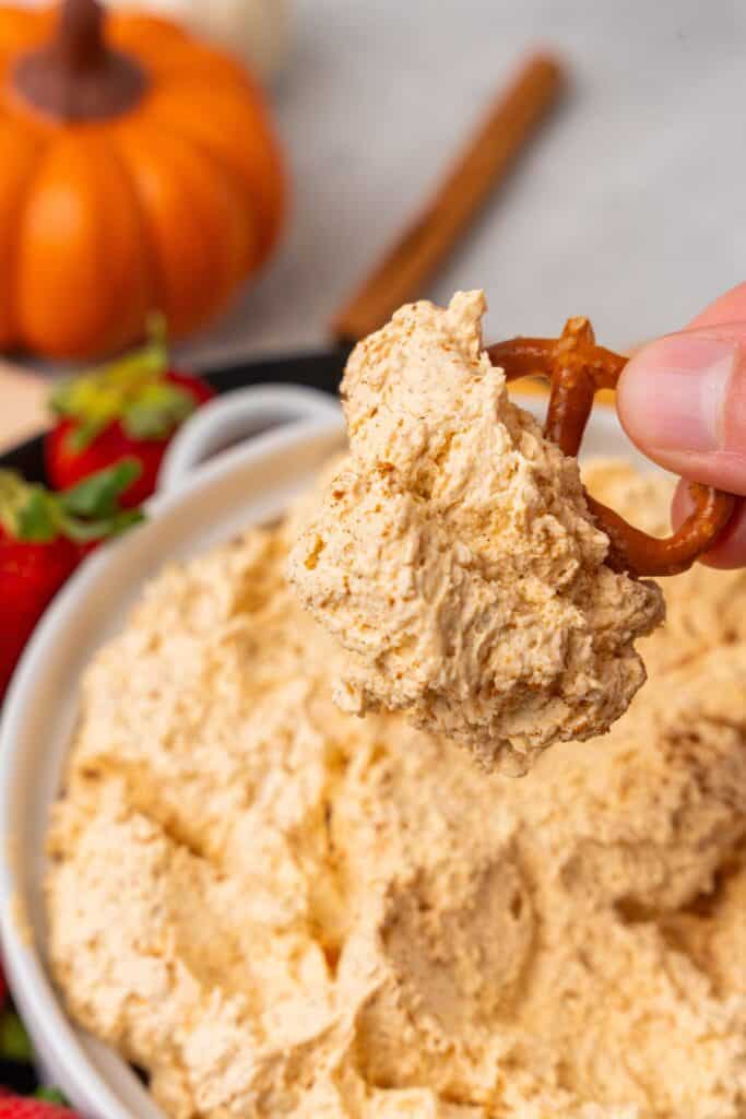 A pretzel being dipped into the pumpkin cream cheese dip to see the fluffy texture of the dip.