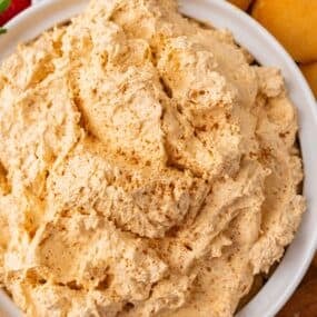 Pumpkin dip with Cool Whip in a serving bowl with Nilla wafers, strawberries, and pretzels around it.