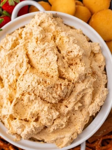 Pumpkin dip with Cool Whip in a serving bowl with Nilla wafers, strawberries, and pretzels around it.