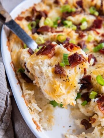 Twice baked mashed potatoes in a casserole dish being scooped out with a serving spoon.