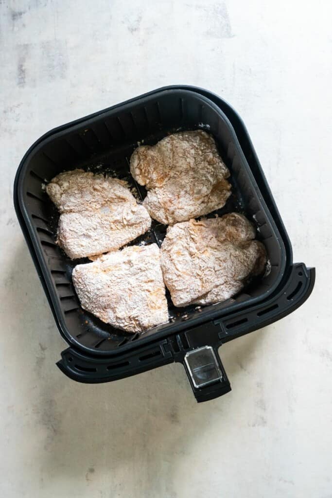adding coated chicken breasts into air fryer basket 