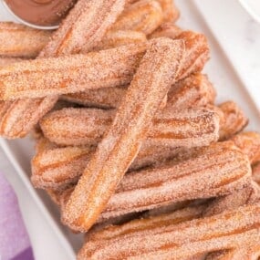 air fryer churros stacked on top of each other with dipping sauce