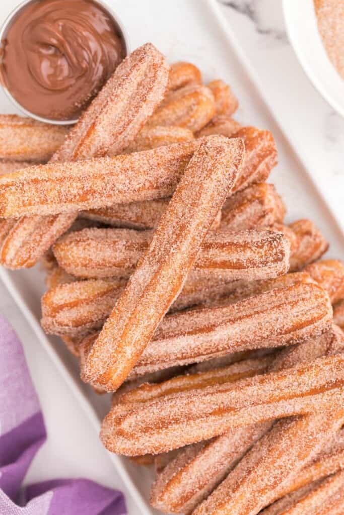 air fryer churros stacked on top of each other with dipping sauce