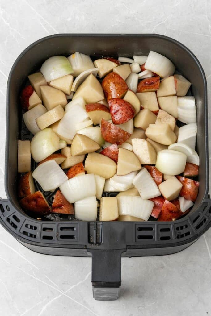 adding raw potatoes and onions to an air fryer basket 