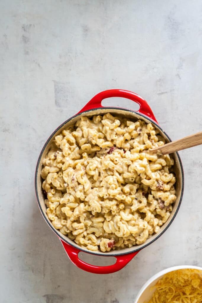 mixing in cooked pasta and crispy bacon with homemade cheese sauce