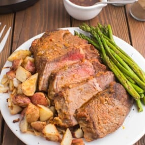 sliced tri tip on a white plate with roasted potatoes and asparagus