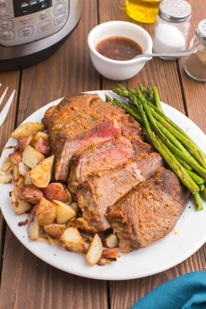 sliced tri tip on a white plate with roasted potatoes and asparagus 