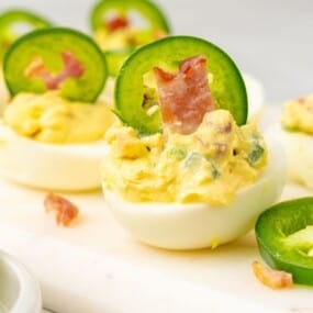 Close up of two jalapeno popper deviled eggs on a white cutting board.